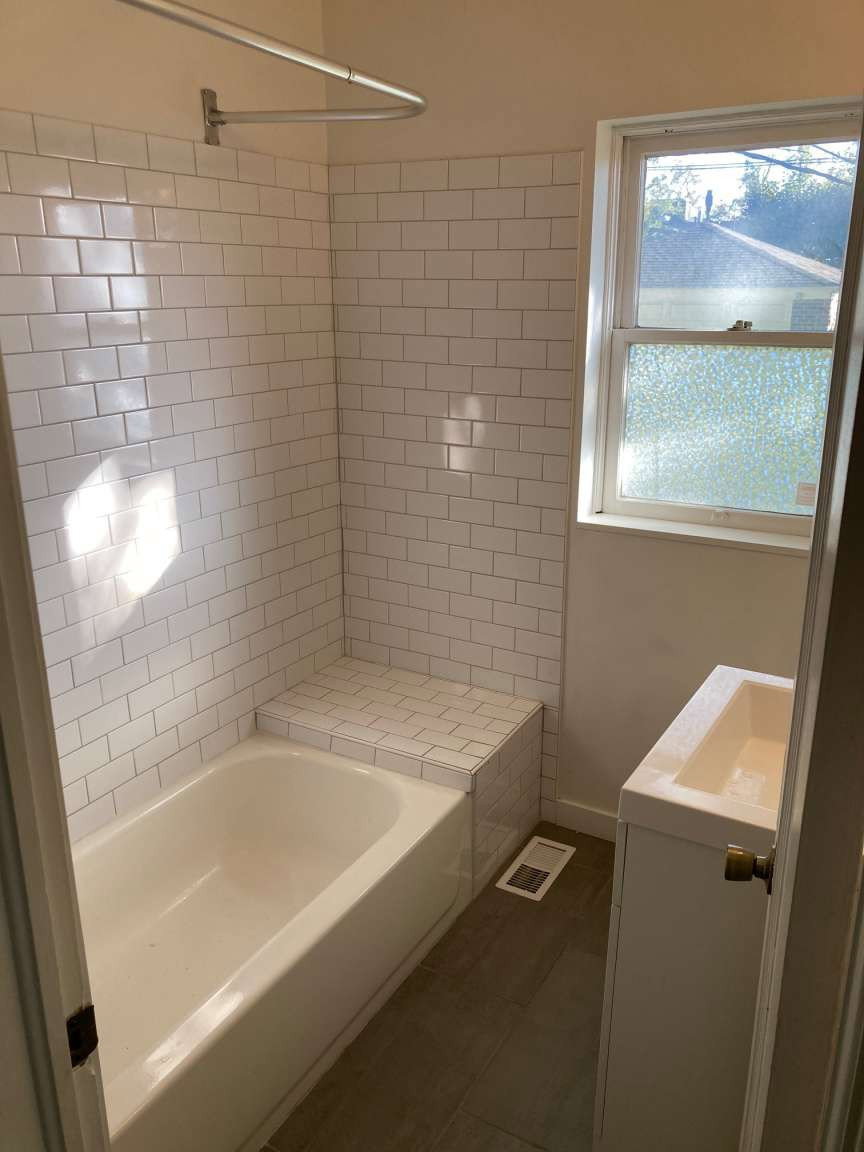 Bathroom featuring a white subway tile surround, a built-in tiled bench, a bathtub with shower rod, a single-sink vanity with cabinet storage, and wood-finish flooring