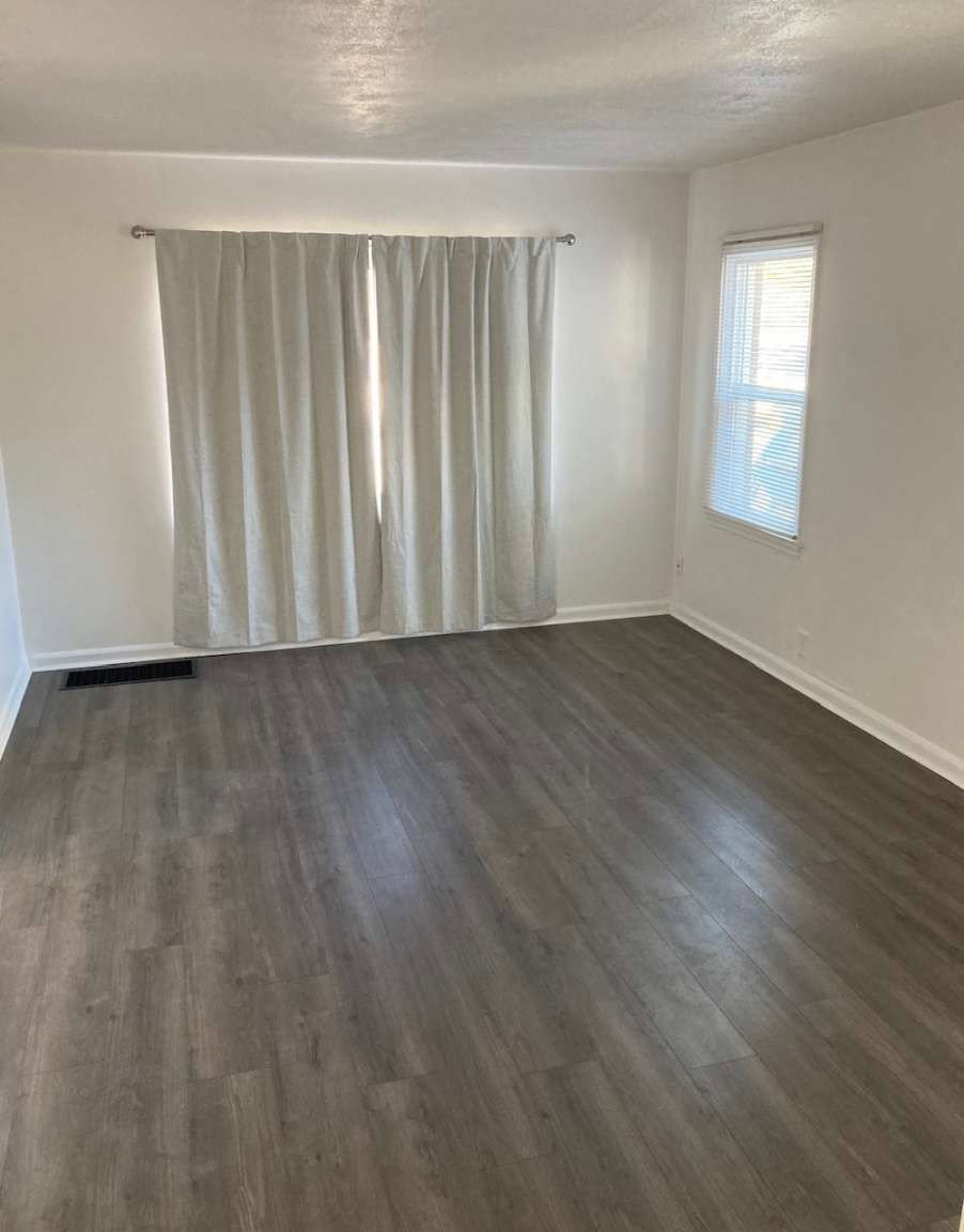 Spacious interior room featuring wood-finish flooring, white baseboards, and two windows