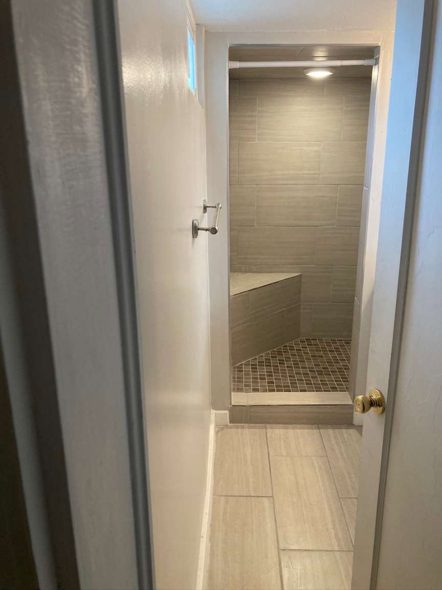 Shower enclosure featuring large format tile walls, mosaic tile floor, built-in bench, and recessed ceiling lighting