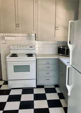 Kitchen featuring dark floors, white appliances, decorative backsplash, gray cabinets, and tile counters