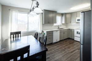 Kitchen featuring gray cabinetry, white appliances, backsplash, decorative light fixtures, and dark wood finished floors