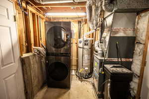 Washroom with concrete floors, secured water heater, heating unit, and stacked washer and clothes dryer