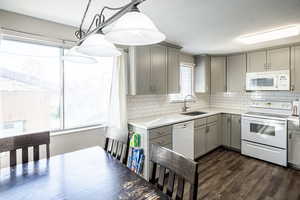 Kitchen with gray cabinetry, white appliances, healthy amount of natural light, and hanging light fixtures
