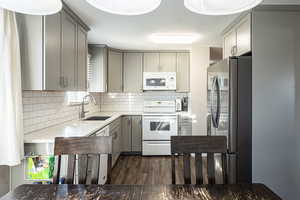 Kitchen featuring gray cabinetry, white appliances, light stone countertops, tasteful backsplash, and dark wood-type flooring