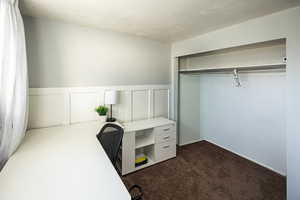 Home office featuring a decorative wall, dark colored carpet, and wainscoting