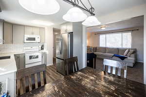 Kitchen with white appliances, light stone countertops, tasteful backsplash, pendant lighting, and open floor plan