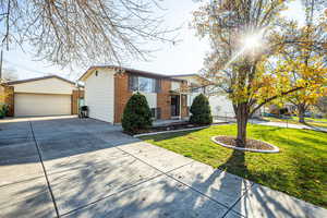 View of front facade featuring a front lawn, brick siding, an outbuilding, and a detached garage