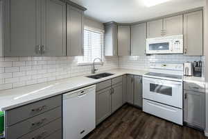 Kitchen with gray cabinets, white appliances, light stone countertops, tasteful backsplash, and dark wood-style flooring