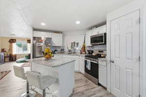 Kitchen featuring a kitchen breakfast bar, appliances with stainless steel finishes, white cabinets, light stone countertops, and recessed lighting
