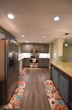 Kitchen featuring appliances with stainless steel finishes, hanging light fixtures, dark wood-style flooring, light stone countertops, and recessed lighting
