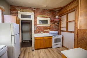 Kitchen with brick wall, brown cabinetry, white appliances, light countertops, and light wood-style flooring