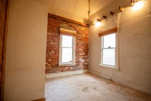 Carpeted spare room featuring a textured wall, healthy amount of natural light, and brick wall