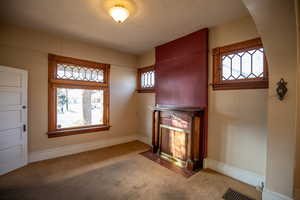 Unfurnished living room featuring healthy amount of natural light, carpet floors, a fireplace with flush hearth, and a textured ceiling