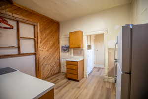 Kitchen featuring freestanding refrigerator, light countertops, light wood-style floors, brown cabinets, and wooden walls