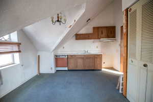 Kitchen with vaulted ceiling, brown cabinets, light countertops, a chandelier, and dark colored carpet