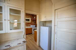 Kitchen with light countertops, white appliances, white cabinetry, glass insert cabinets, and light wood-type flooring