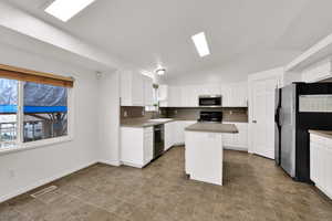 Kitchen featuring vaulted ceiling, stainless steel appliances, a center island, white cabinets, and light countertops