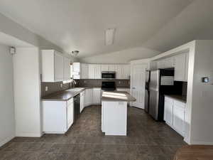 Kitchen with vaulted ceiling, white cabinetry, a center island, and stainless steel appliances