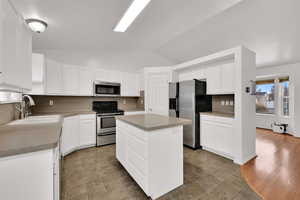 Kitchen with stainless steel appliances, vaulted ceiling, white cabinetry, a center island, and light countertops