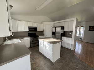 Kitchen with appliances with stainless steel finishes, white cabinetry, vaulted ceiling, a center island, and dark countertops
