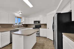 Kitchen featuring vaulted ceiling, appliances with stainless steel finishes, white cabinetry, a center island, and light countertops