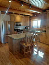Kitchen featuring a wood ceiling with exposed beams, stainless steel appliances, light stone countertops, a breakfast bar, and light wood-style flooring