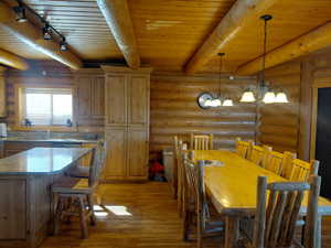 Dining room with light wood-style flooring, rustic walls, a wooden ceiling with exposed beams, a chandelier, and rail lighting