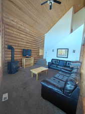 Living room with log walls, a wood stove, wooden ceiling, high vaulted ceiling, and dark colored carpet