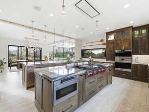 Kitchen with light stone countertops, appliances with stainless steel finishes, dark brown cabinetry, pendant lighting, and tasteful backsplash