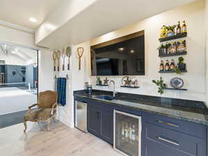 Indoor wet bar featuring dark stone counters, wine cooler, light wood-style flooring, stainless steel fridge, and open shelves