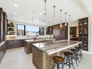 Kitchen featuring dark brown cabinetry, dark stone countertops, decorative light fixtures, a kitchen breakfast bar, and light tile patterned flooring