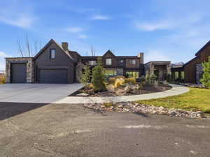 View of front facade with stone siding, driveway, a garage, a chimney, and board and batten siding