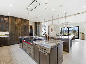 Kitchen featuring glass insert cabinets, dark brown cabinetry, light stone countertops, and recessed lighting