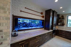 Kitchen with open shelves, dark brown cabinets, light stone countertops, recessed lighting, and light tile patterned floors