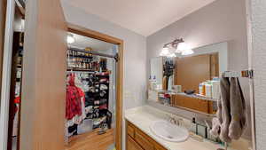 Bathroom with vanity, a spacious closet, light wood finished floors, a chandelier, and a textured wall
