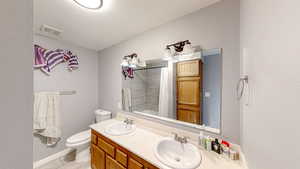 Bathroom featuring tiled shower, double vanity, and a textured wall