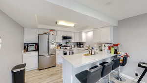 Kitchen featuring a tray ceiling, stainless steel appliances, a kitchen bar, and a peninsula