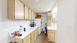 Kitchen with light brown cabinetry, light countertops, freestanding refrigerator, black microwave, and light colored carpet