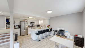 Kitchen with light countertops, appliances with stainless steel finishes, a kitchen breakfast bar, white cabinetry, and light wood-type flooring