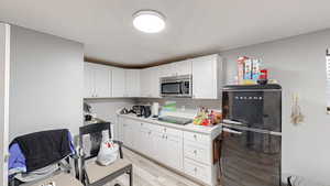 Kitchen with light countertops, black appliances, light wood-style floors, and white cabinets