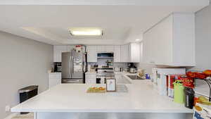 Kitchen featuring a tray ceiling, stainless steel appliances, white cabinets, a peninsula, and a kitchen breakfast bar