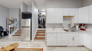 Kitchen with freestanding refrigerator, light countertops, white cabinets, and light wood-style flooring