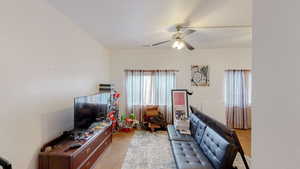Living area featuring a textured wall, light colored carpet, and a ceiling fan