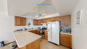 Kitchen featuring a peninsula, a tray ceiling, light countertops, appliances with stainless steel finishes, and a textured ceiling