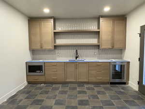 Bar area featuring decorative backsplash, light countertops, open shelves, beverage cooler, and stainless steel microwave