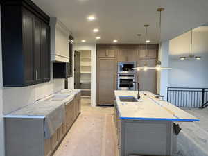Kitchen with stainless steel appliances, a center island with sink, pendant lighting, and light stone countertops