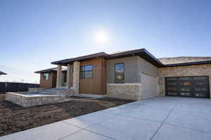 View of front of property featuring stone siding, an attached garage, concrete driveway, and a patio area