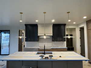 Kitchen with a kitchen island with sink, light stone countertops, decorative light fixtures, and dark cabinets
