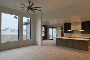 Kitchen featuring an island with sink, decorative light fixtures, light colored carpet, a ceiling fan, and light stone countertops