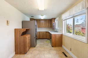 Kitchen with brown cabinets, light countertops, stainless steel appliances, a textured wall, and wallpapered walls